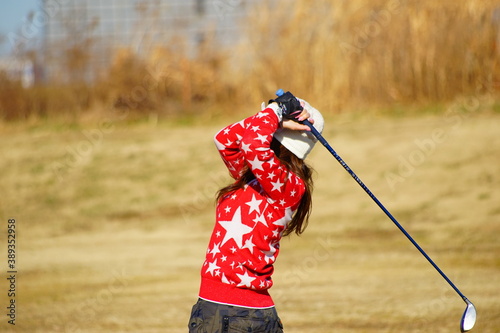 冬のゴルフ場における30歳代の女性ゴルファーのアイアンショットのフォロースルー