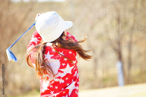 冬のゴルフ場における赤いセーターを着た30歳代の女性ゴルファーのアイアンショットのフォロースルー