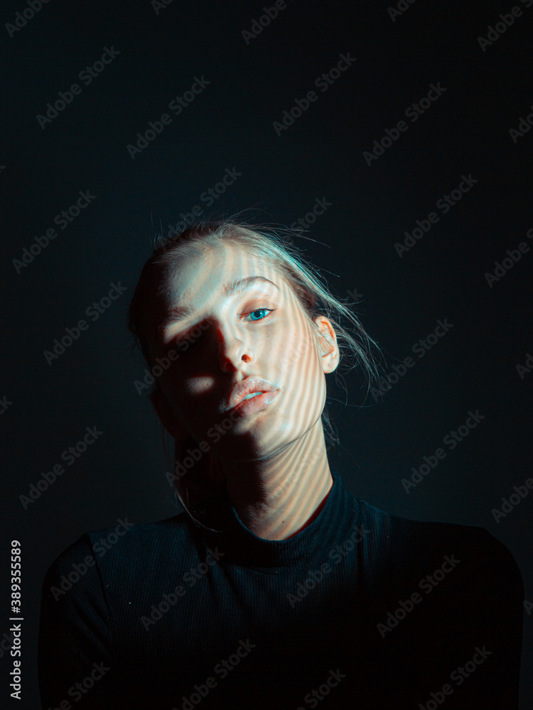 Fototapeta premium Portrait of beautiful young girl with a shadow pattern on her face in black dark studio