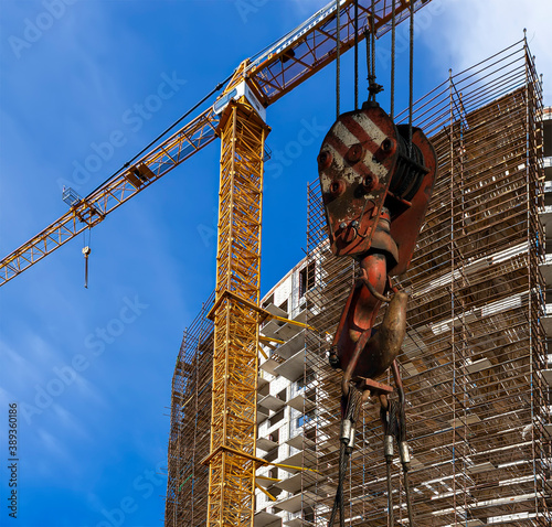 Construction crane hook with multi-storey building under construction with scaffolding (new residential complex) on the background, Moscow, Russia © Владимир Журавлёв
