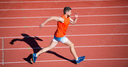 athletic muscular male running on racetrack at outdoor stadium, competition