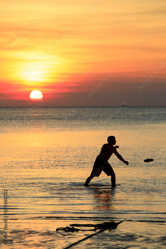 man playing beach flying disc against beautiful sunset sky