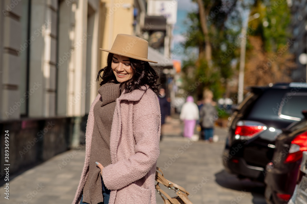 Fototapeta premium beautiful caucasian brunette woman in a stylish outfit walking down the street in the offseason in a coat and hat
