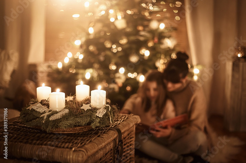 Child sits with mother in front of the Christmas tree and read a book together and look forward to Christmas, advent wreath photo