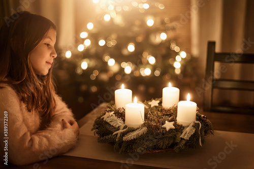 Child sits alone in front of a glowing Advent wreath and looks forward to Christmas. Girls, candles, warm photo