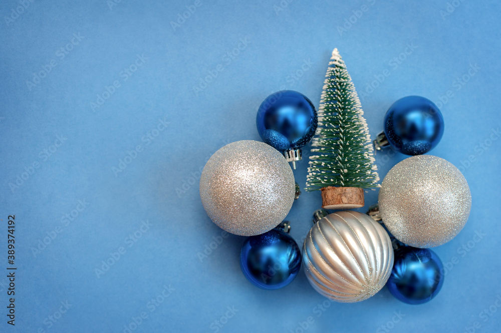 Silver and blue Christmas balls and a small Christmas tree on a blue background