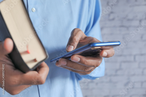 close up of man using smart phone and holding a book 