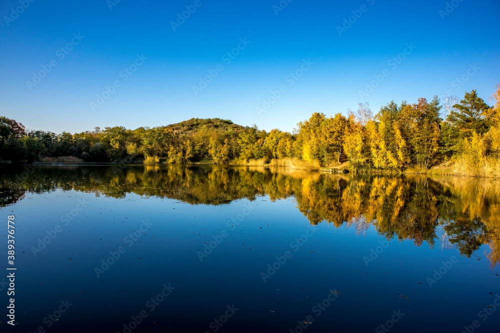 A beautiful little lake called Schnepfensee in Germany at a sunny day in Autumn with a colorful forest reflecting in the water. A beautiful little lake called Schnepfensee in Germany at a sunny day in Autumn with a colorful forest reflecting in the water.