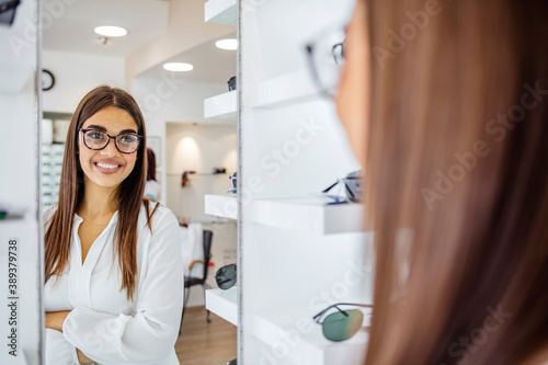 Health care, eyesight and vision concept - happy woman choosing glasses at optics store. Woman looking with glasses in mirror at optician store Free Download Health care, eyesight and vision concept - happy woman choosing glasses at optics store. Woman looking with glasses in mirror at optician store - GFXLoad