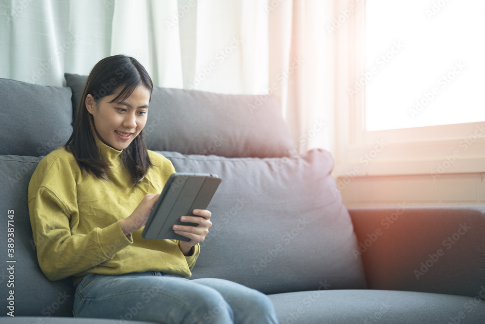 Fototapeta premium An Asian woman sitting on a tablet on a sofa