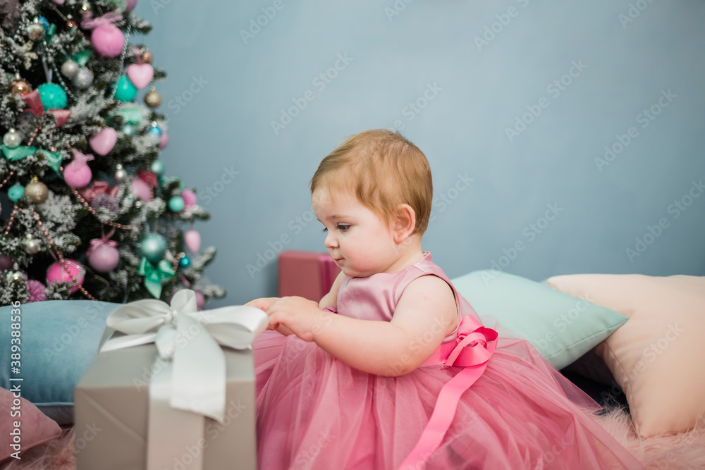 portrait of a little girl in a festive pink dress opening a gift on the background of a Christmas tree portrait of a little girl in a festive pink dress opening a gift on the background of a Christmas tree