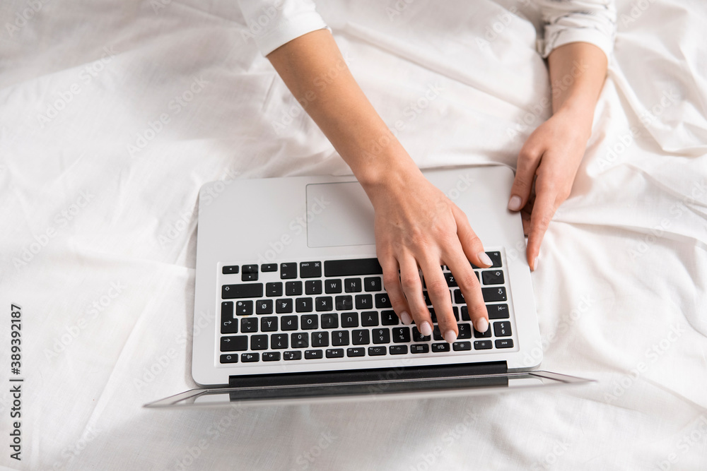 Top view of a woman sitting on a bed , using laptop. Working at home concept. Girl is working on her laptop in bed with white linens. Relaxing working process. Stay at home. Top view of a woman sitting on a bed , using laptop. Working at home concept. Girl is working on her laptop in bed with white linens. Relaxing working process. Stay at home.