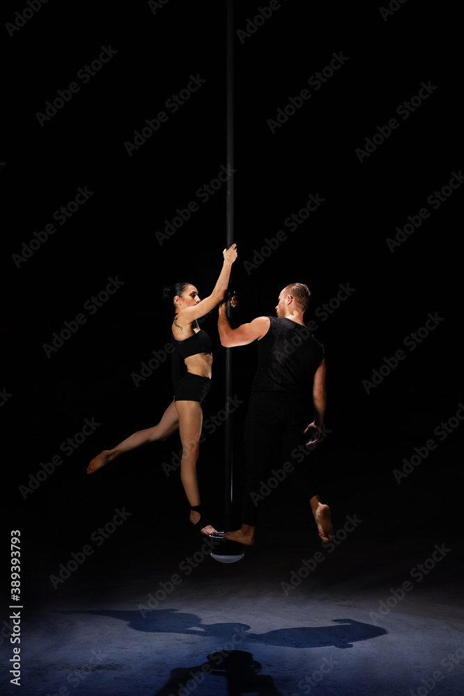 Man and woman doing exercises on pylon isolated on black background.Pole dance concept. Man and woman doing exercises on pylon isolated on black background.Pole dance concept.