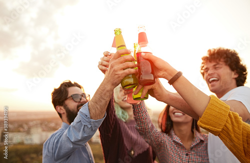 Happy friends clinking beer bottles at sunset