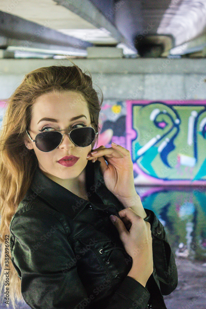 Russia, Korolev - 08/27/2019: Biker girl with glasses against a background of graffiti.