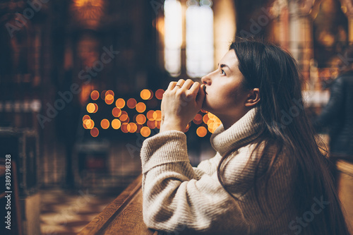 a young pretty woman came to the temple to pray to God. The parishioner of the church sits on a bench with her hands folded for prayer and heartily prays. copy space