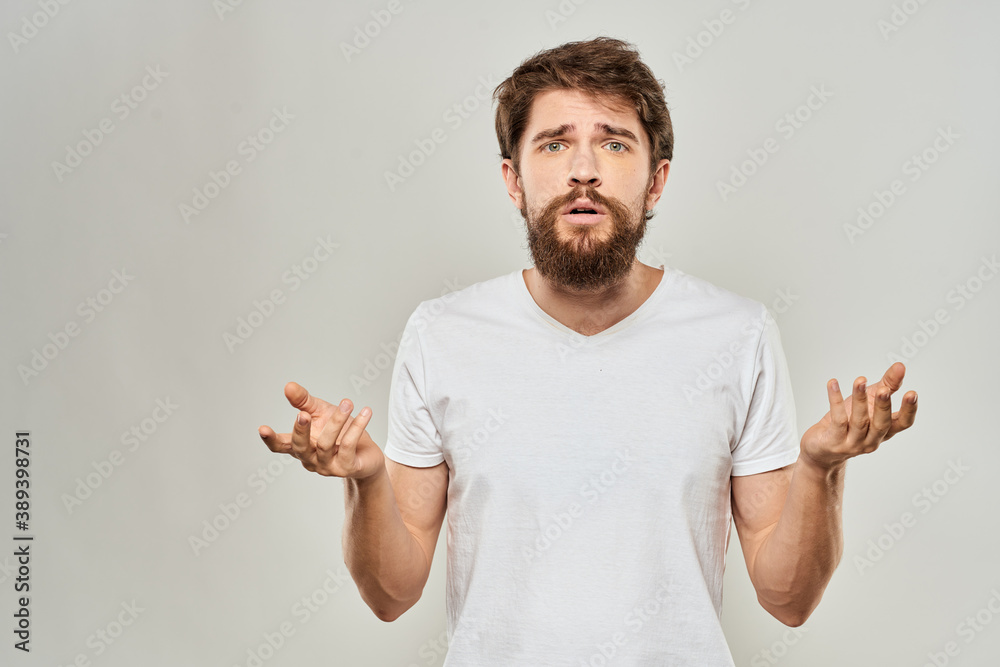 A man in a white t-shirt with a beard emotions displeased facial expression light background A man in a white t-shirt with a beard emotions displeased facial expression light background