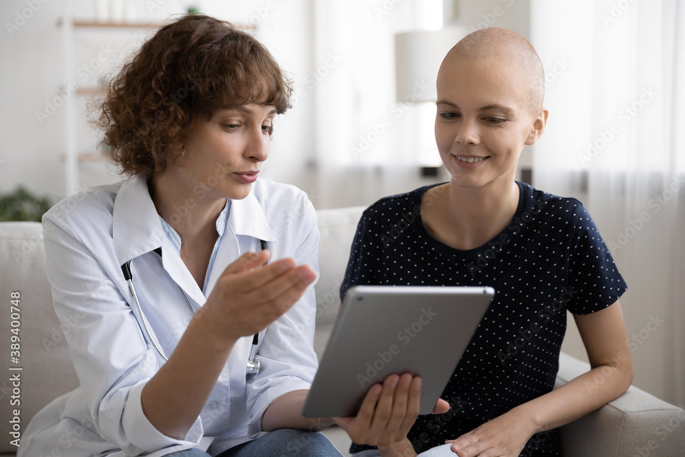 Close up doctor consulting hairless woman about medical checkup result, holding computer tablet, sitting on couch in hospital, nurse explaining treatment plan, young female struggling with cancer Close up doctor consulting hairless woman about medical checkup result, holding computer tablet, sitting on couch in hospital, nurse explaining treatment plan, young female struggling with cancer