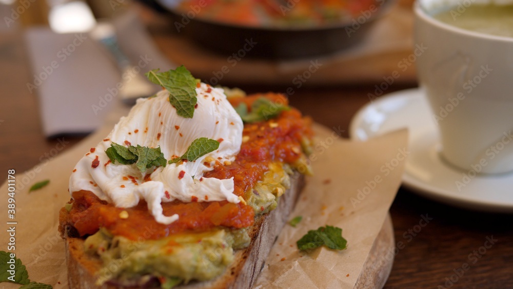 Healthy vegetarian Mediterranean brunch out. Avocado toast with poached egg and tomato paste on wooden plate with coffee Healthy vegetarian Mediterranean brunch out. Avocado toast with poached egg and tomato paste on wooden plate with coffee