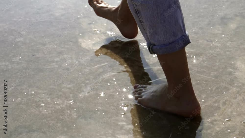 Woman feet walking barefoot by lake or sea shore in lins flares
