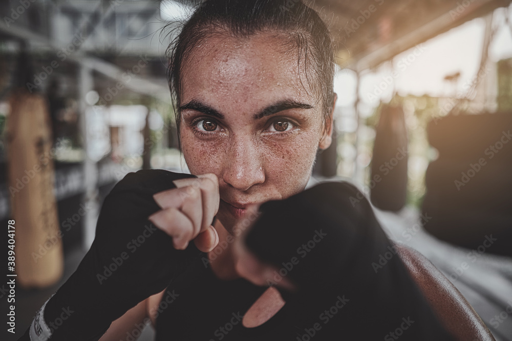 Portrait of a woman standing in striking pose and looking at camera at dark ring. Portrait of woman kickboxer ready to punch. Muay thai concept