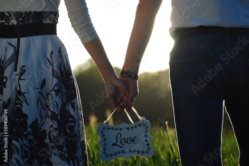 zakochani kobieta i mężczyzna spacerując po łące w wysokiej trawie podczas zachodu słońca, wspólnie trzymając, niosą w dłoniach białą tabliczkę z napisem love