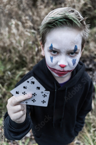  A boy in a Joker costume. A teenager in makeup with cards in his hands.