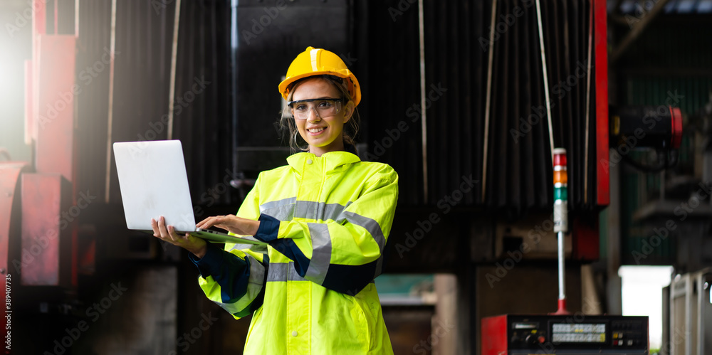 Female Quality control inspector checking workers at factory. Woman engineer with yellow hard hat helmet working on laptop computer inside industrial manufacturing factory