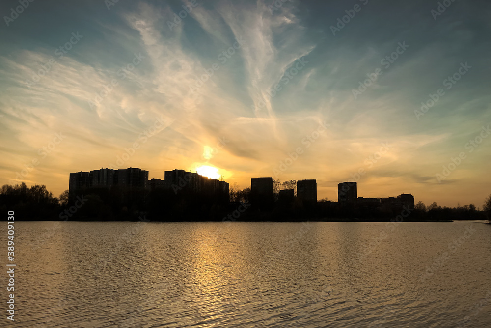 Rippled water surface of lake with city buildings silhouettes on the horizon at sunset