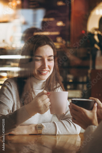 young pretty girl with a big pink mug of sweet coffee sits on a chair in her favorite cafe and drinks her daily morning coffee and talks with a girlfriend