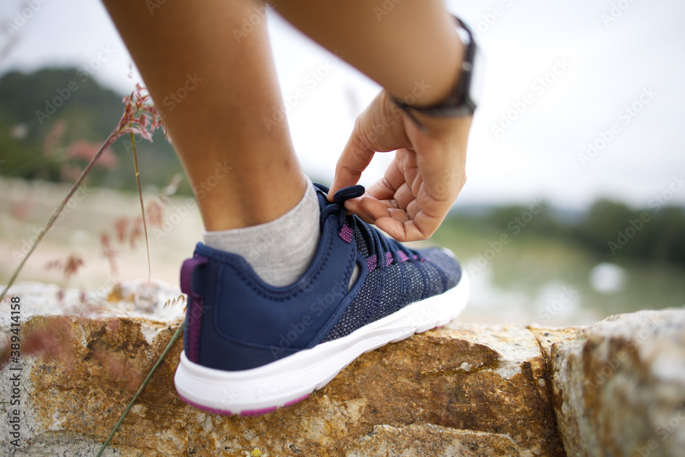 The woman stepped on the rock and tying her shoes to prepare for running in the adventure activity.