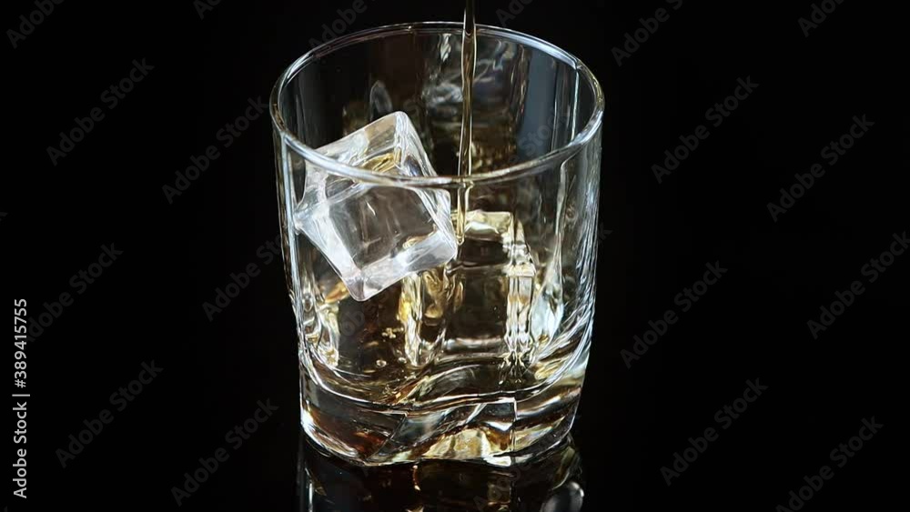 whiskey pouring into glass on black background whiskey pouring into glass on black background