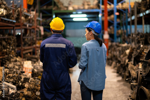 Engineer man and administrator standing in the automotive parts warehouse. Keep the old machine parts. Wearing a safety helmet. Used of vehicle part for recycling in the scrap yard garage. .