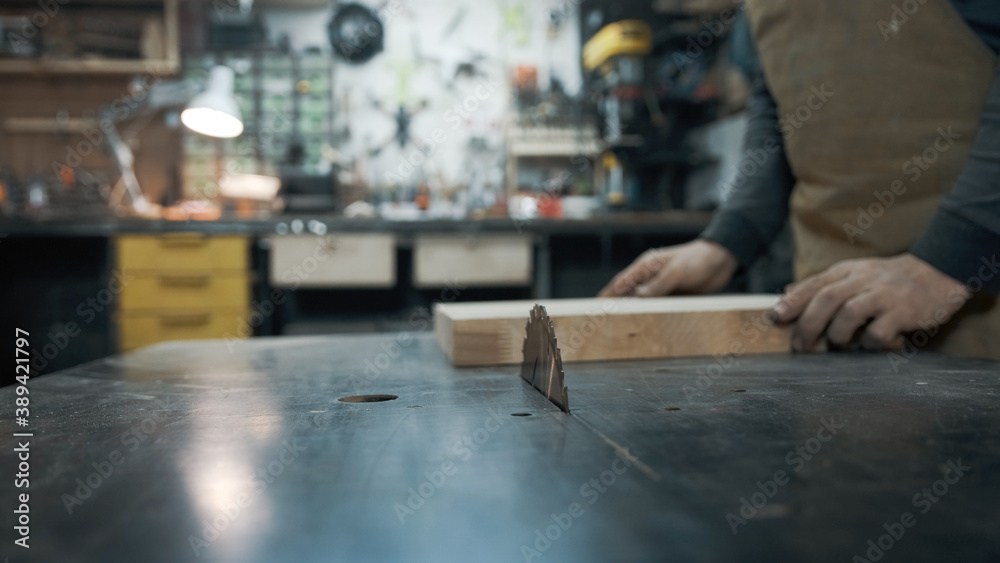 A carpenter wearing an apron and a mask is sawing a tree on a circular saw in a workshop A carpenter wearing an apron and a mask is sawing a tree on a circular saw in a workshop