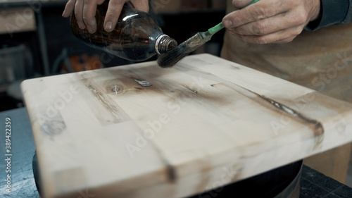 A carpenter paints a piece of wood for a loft-style chair with a brush. Close up