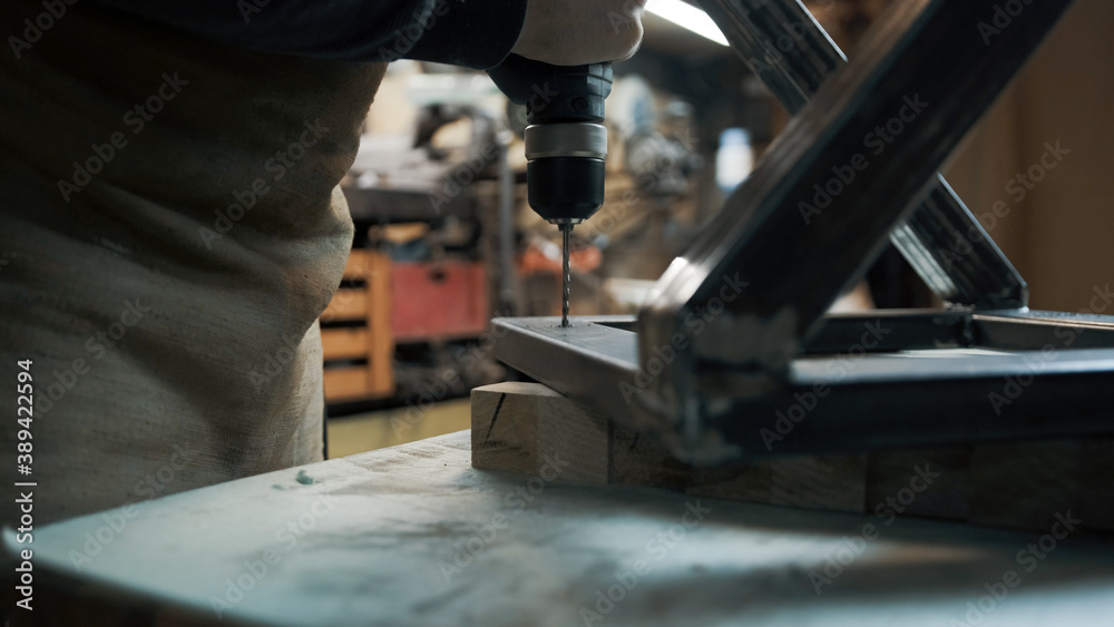 Man drills a hole with a screwdriver in the metal frame of a loft-style chair Man drills a hole with a screwdriver in the metal frame of a loft-style chair