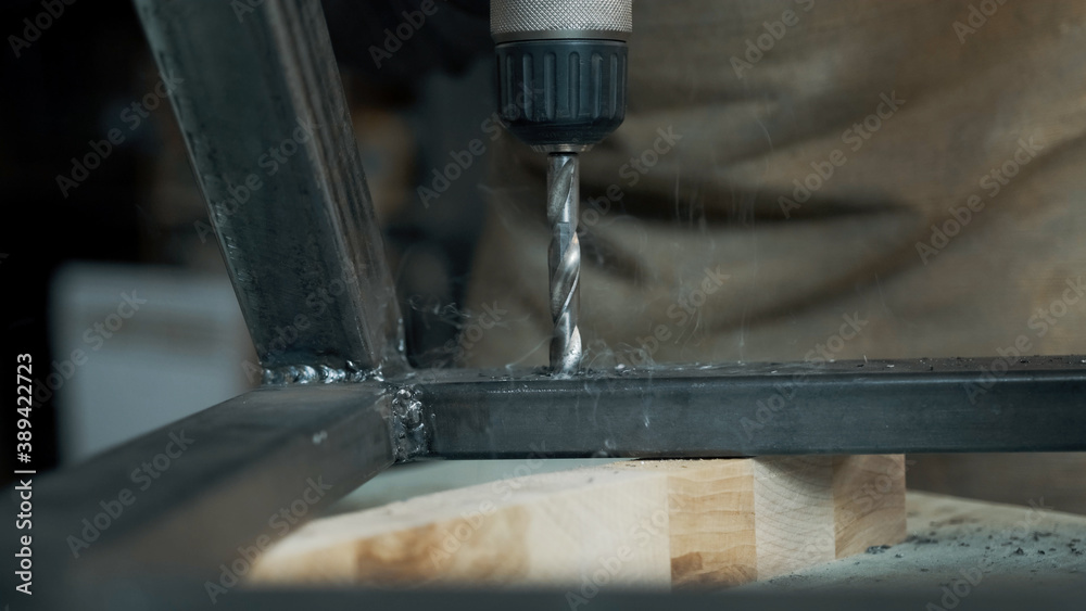 Man drills a hole with a screwdriver in the metal frame of a loft-style chair