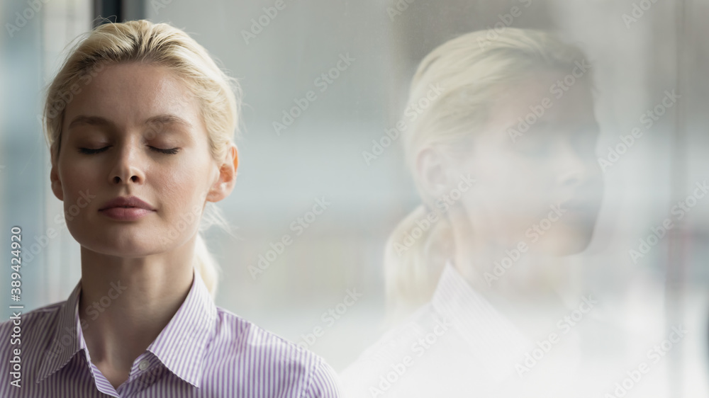 Head shot close up mindful young businesswoman breathing fresh air with closed eyes near window, enjoying calm break pause time in office, reducing stress pressure during workday, copy space for text. Head shot close up mindful young businesswoman breathing fresh air with closed eyes near window, enjoying calm break pause time in office, reducing stress pressure during workday, copy space for text.
