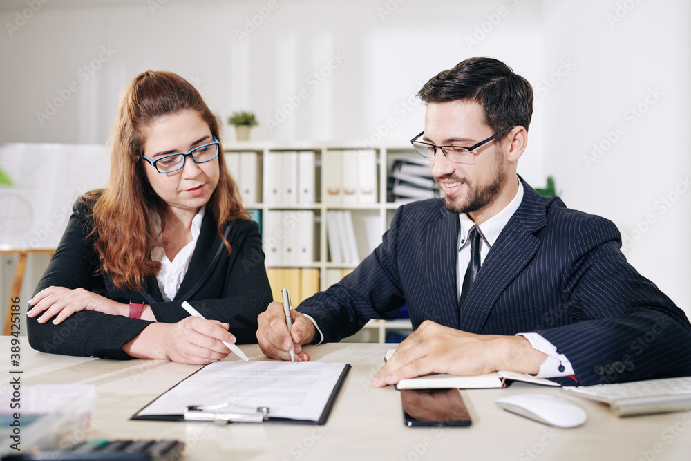 Positive business partners in glasses discussing every sentence in contract before signing it Positive business partners in glasses discussing every sentence in contract before signing it