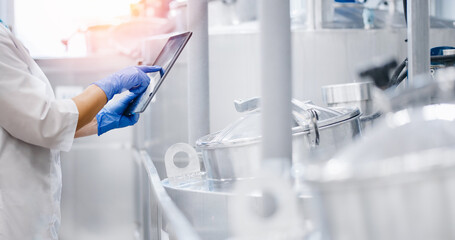 Concept food industry banner. Factory worker inspecting production line tanker in of dairy factory with computer tablet