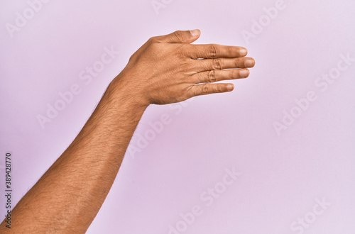 Arm and hand of caucasian young man over pink isolated background stretching and reaching with open hand for handshake, showing back of the hand