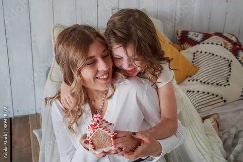 Mother and daughter in beautiful dress sittig on bed with gingerbread house photo