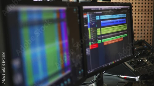 Dual monitor setup at an audio recording studio with a daw with mutliple audio channels and a digital mixer. Shot in 4K. Racking Focus.
