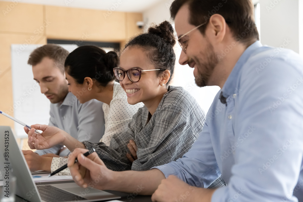 Head shot happy smiling multiracial colleagues sitting at desk with computers, working on different project parts in groups, communicating discussing brainstorming ideas m using software apps.