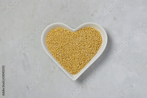 Raw pasta ptitim on heart-shaped plate on gray table. Top view. Horizontal format