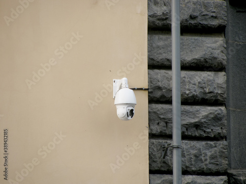A white street surveillance camera hangs on the wall outside