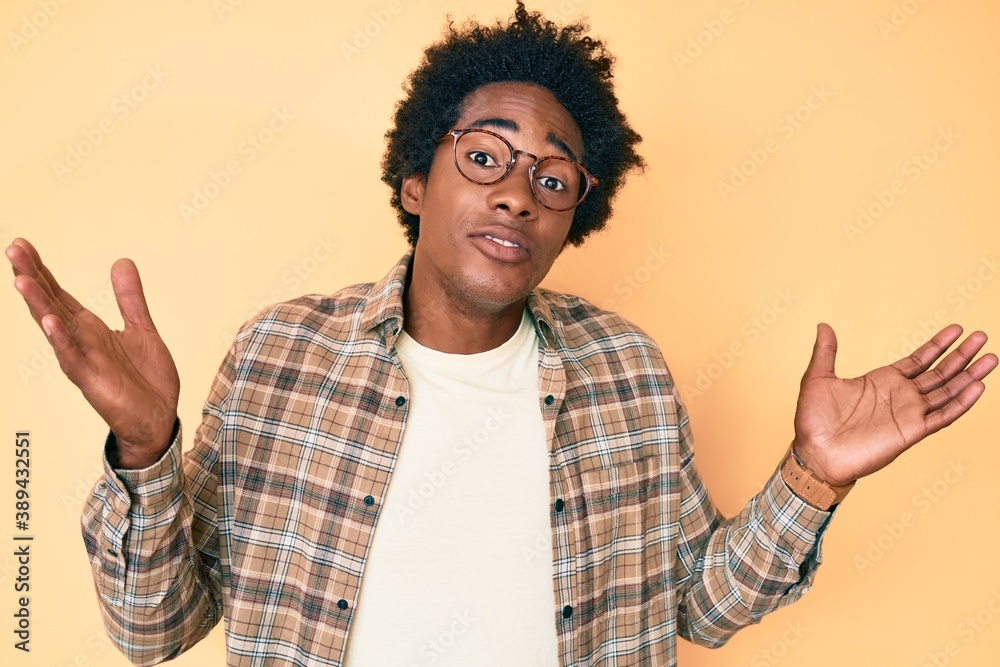 Handsome african american man with afro hair wearing casual clothes and glasses clueless and confused with open arms, no idea and doubtful face. Handsome african american man with afro hair wearing casual clothes and glasses clueless and confused with open arms, no idea and doubtful face.