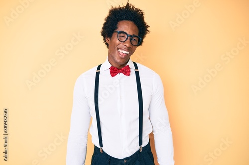 Handsome african american man with afro hair wearing hipster elegant look winking looking at the camera with sexy expression, cheerful and happy face.