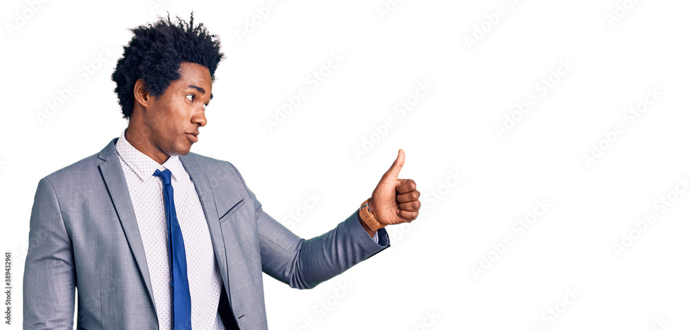Handsome african american man with afro hair wearing business jacket looking proud, smiling doing thumbs up gesture to the side Handsome african american man with afro hair wearing business jacket looking proud, smiling doing thumbs up gesture to the side