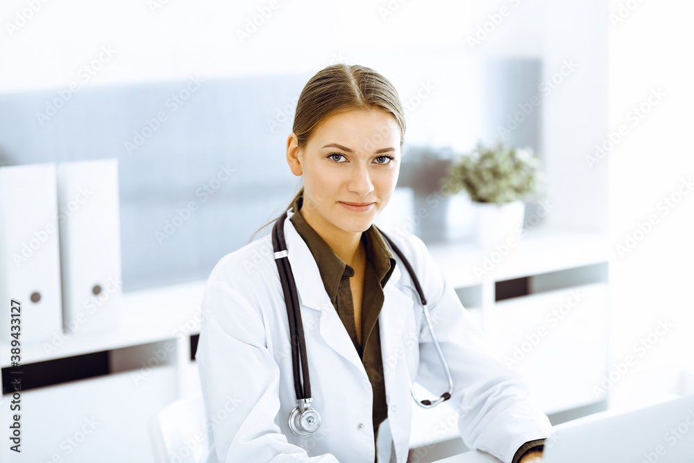 Woman-doctor typing on laptop computer while sitting at the desk in hospital office. Physician at work Woman-doctor typing on laptop computer while sitting at the desk in hospital office. Physician at work